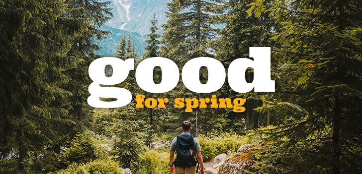 Person hiking in the woods looking towards a mountain in the background. Good For Spring text overlaying image